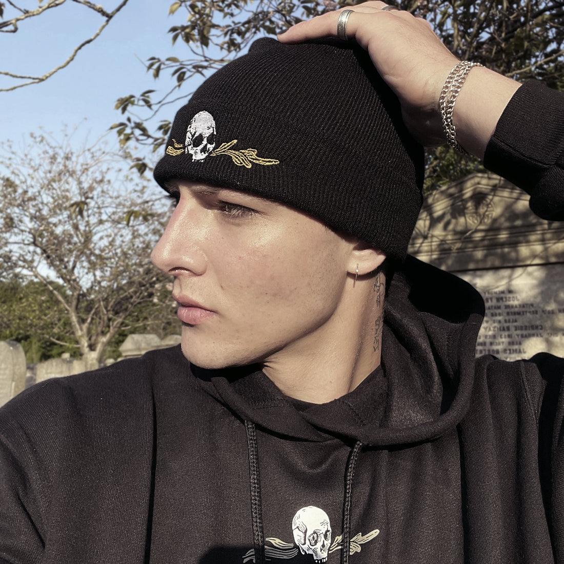 Person wearing a black beanie and hoodie with skull designs outdoors.