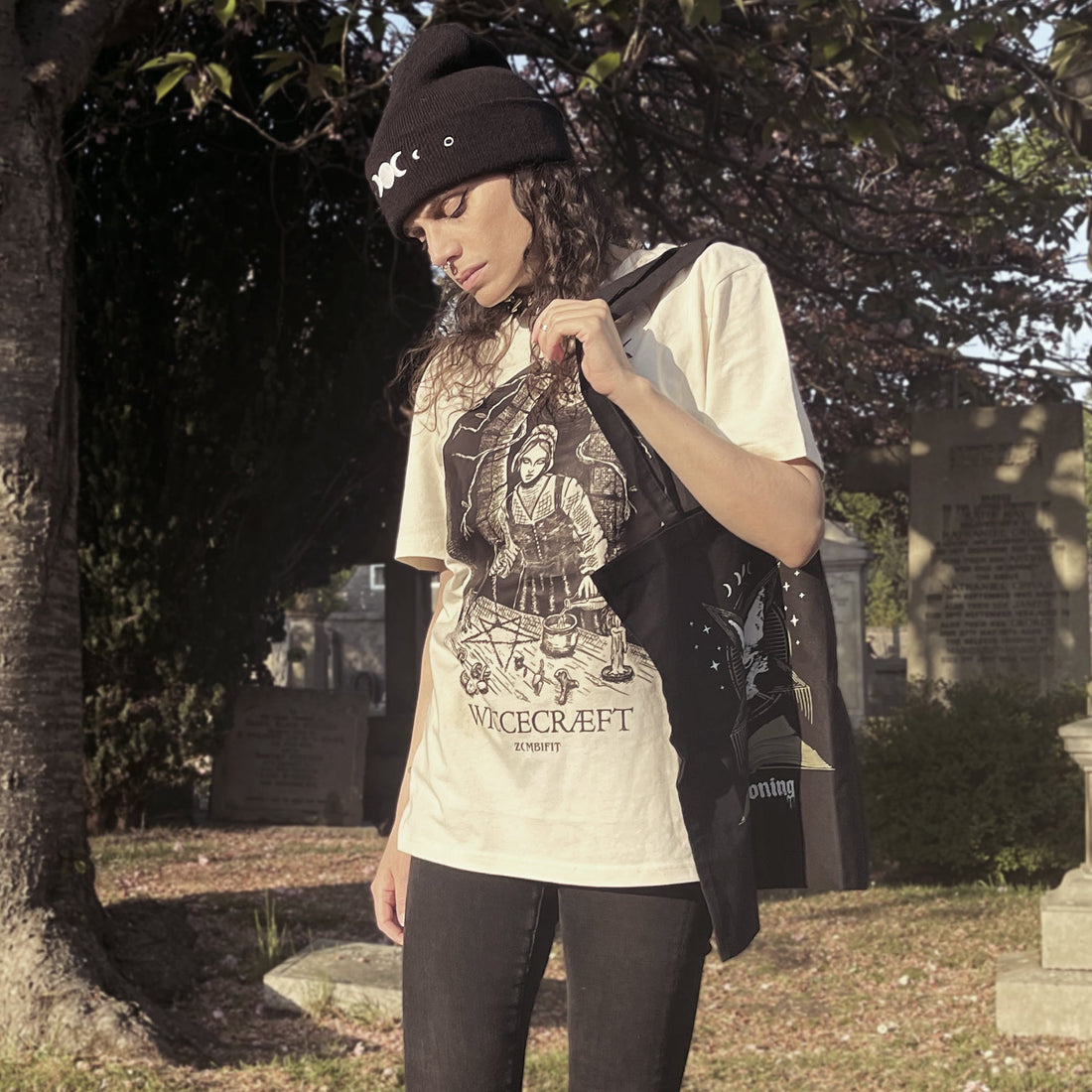 Person wearing a white t-shirt with a graphic design and text, standing in a cemetery.